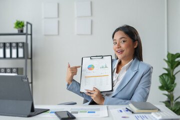 Asian businesswoman is pointing at charts on a clipboard while working at her desk in an office