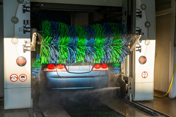 Car going through an automated car wash machine, being cleaned by green and blue brushes and spraying water