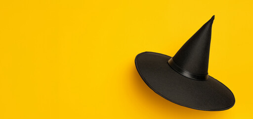 Fototapeta premium Black witch hat on bright yellow background. Minimalist style, Halloween concept. Image for banner with copy space, poster, and social media.