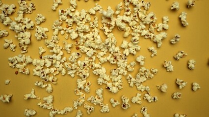 Slow motion shot of popcorn was throwing with yellow background. Fresh movie popcorn moving and falling. Popcorn in motion falling in a captivating dance. Dynamic movement and energy. Comestible.