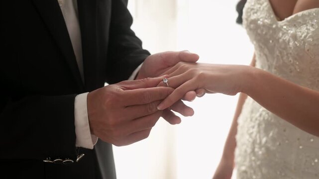 Close up of Groom putting diamond engagement ring on bride's finger in wedding ceremony
