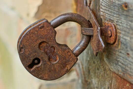 one rusty industrial old iron secure retro brown closed security padlock hanging on a shackle on wooden doors