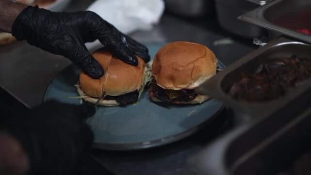 A chef with black gloves cutting smashed burgers in half


