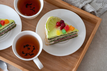 Two slices of fruit cake with citrus and berry toppings, placed beside cups of tea on a wooden tray, creating a cozy and inviting setting