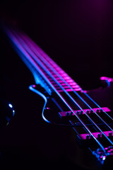 Electric bass guitar strings illuminated with purple and blue lights, dark background