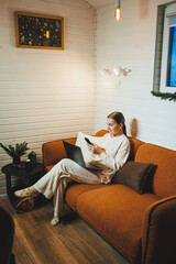 Obraz premium A woman in home clothes is sitting at home on the sofa with a laptop and talking on the phone. Work from home.