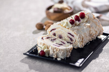 Sliced cream roll with berries on a black plate, dusted with powdered sugar.