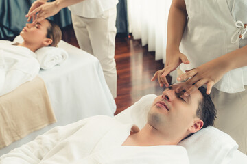 Caucasian couple enjoying relaxing anti-stress head massage and pampering facial beauty skin recreation leisure in dayspa modern light ambient at luxury resort or hotel spa salon. Quiescent