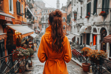 Obraz premium Portrait of a young brunette woman in a warm autumn orange coat against the background of the city. Back view