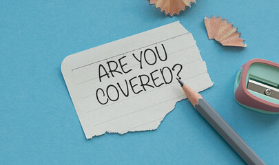 ARE YOU COVERED text written on paper notebook with pencil on blue background