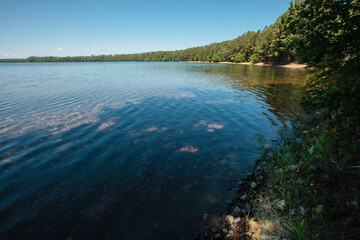 The northern shoreline of Trout Lake near Boulder Junction, Wisconsin, curves west on the eastern side as the calm waters allow the rocks of the shallow waters to be seen.