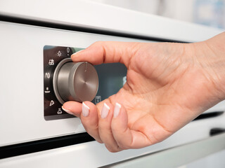 Woman adjusting modern white oven in kitchen.  Female hand pushing and turning knobs on oven...