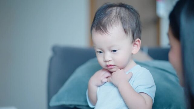 Curious asian boy preschooler sitting next to the couch while listening to story from the book, young adult asian female reading book for her child, kids development skills, fast learner age
