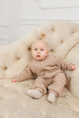 Fototapeta premium A child in beige overalls is sitting on a sofa. Warm clothes for babies