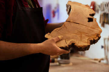 Man in woodworking shop inspecting lumber piece before assembling furniture, checking for...