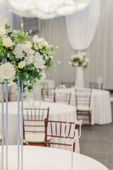 Decorated interior for festive event. Fancy table set for dinner with white flower composition in restaurant, luxury interior background. Wedding elegant banquet decoration arranged by catering