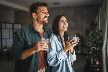 Portrait of couple stand with coffee and water, watch intro the window