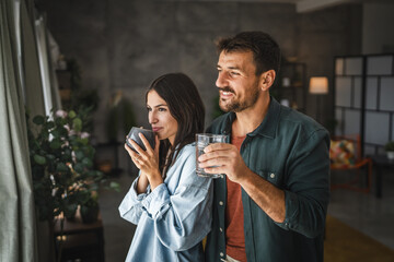 Portrait of couple stand with coffee and water, watch intro the window