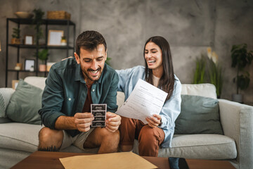 Adult couple sit on sofa and hold ultrasound picture of baby