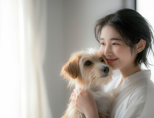 白いシーズー犬を抱きしめる若いアジア人女性。白い部屋の窓辺。