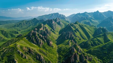 Aerial view of lush green mountains with rocky peaks and clear blue sky, breathtaking landscape scenery