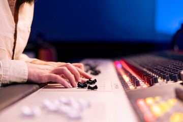 Music producer pushing faders and sliders on control panel board in studio, adjusting volume levels...