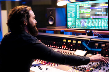 Audio technician operating daw software for mixing and mastering tunes in studio, editing music on control panel board. Skilled producer composing records with faders and switchers.