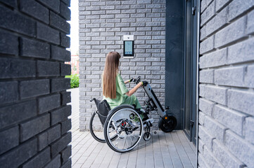 A woman in a wheelchair with an assistive device for manual control enters the entrance. Electric...