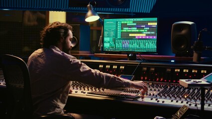 Music producer editing sounds with mixing console and switchers to remove tonal imbalances or white...