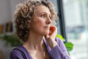 Beautiful mature woman looking forwards near the window in the living room at home