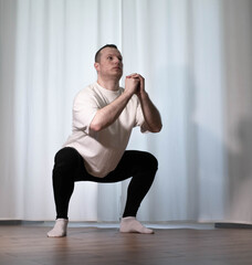 Obraz premium Home workouts in yoga poses. A man performs sports exercises, warming up the body of his arms and legs, A male athlete stretches.