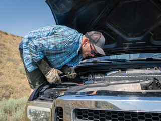 Blue pickup truck breaks down on the shoulder of a freeway while owner tries to assess the problem.