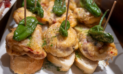 Typical snack of Basque Country, pinchos or pinxtos skewers with small pieces of bread, fish, sea food, sweet green pepper served in bar in San-Sebastian or Bilbao, Spain, close up