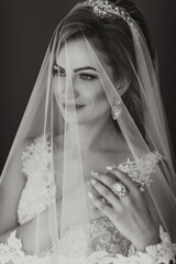 A woman wearing a veil and a ring. She is smiling and looking at the camera. The veil is made of lace and is covering her face