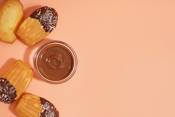 Tasty madeleines and bowl with chocolate paste on orange background