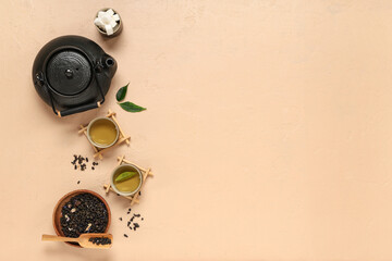 Teapot with cups, wooden bowl of dry tea and sugar on beige background