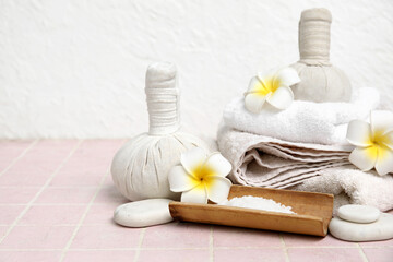 Herbal bags with spa stones, towels, sea salt and plumeria flowers on pink tile table