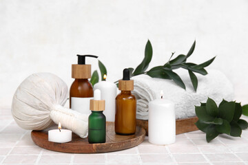 Set of spa supplies with different cosmetic products, herbal bag, towel and burning candles on beige tile table