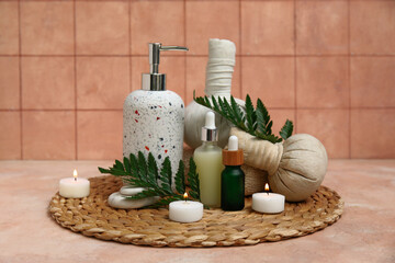 Set of spa supplies with bottles of cosmetic oil, herbal bags, fern branches and burning candles on beige table