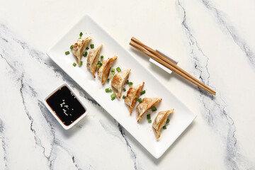 Plate with fried Japanese gyoza and bowl of soy sauce on white background
