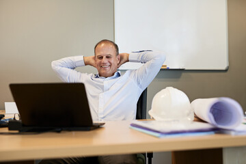 Obraz premium Relax, man and engineer with laptop in office for online site plan approval for construction project. Happy, rest and male industrial architect with hands on head for finished work on computer.