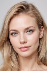 Naklejka premium a close-up portrait of a young woman's face. She has blonde hair that is styled in loose waves and falls over her shoulders. Her eyes are a bright blue color.