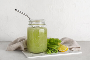 Jar of celery juice with straw, celery and lemon on white background