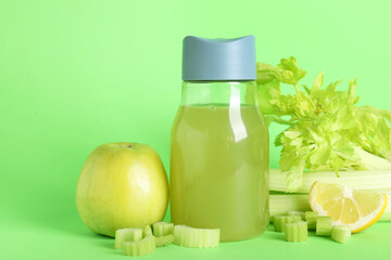 Bottle of celery juice with chopped and whole celery, apple and lemon on green background