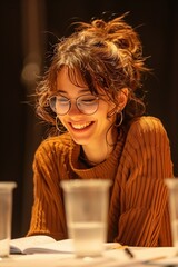 A joyful young woman with glasses smiles while sitting at a table, creating a warm and inviting atmosphere.