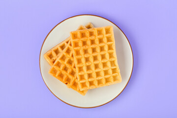 Tasty Belgian waffles in plate on lilac background. Top view