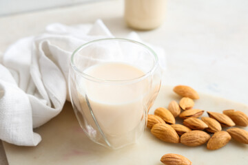 Glass of fresh almond milk and nuts on white background