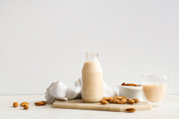 Glass and bottle of fresh almond milk with nuts on white background