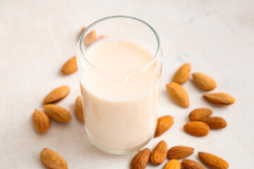 Glass of fresh almond milk and nuts on white background