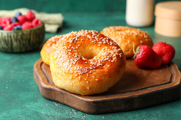 Wooden board with tasty bagels and strawberries on green background